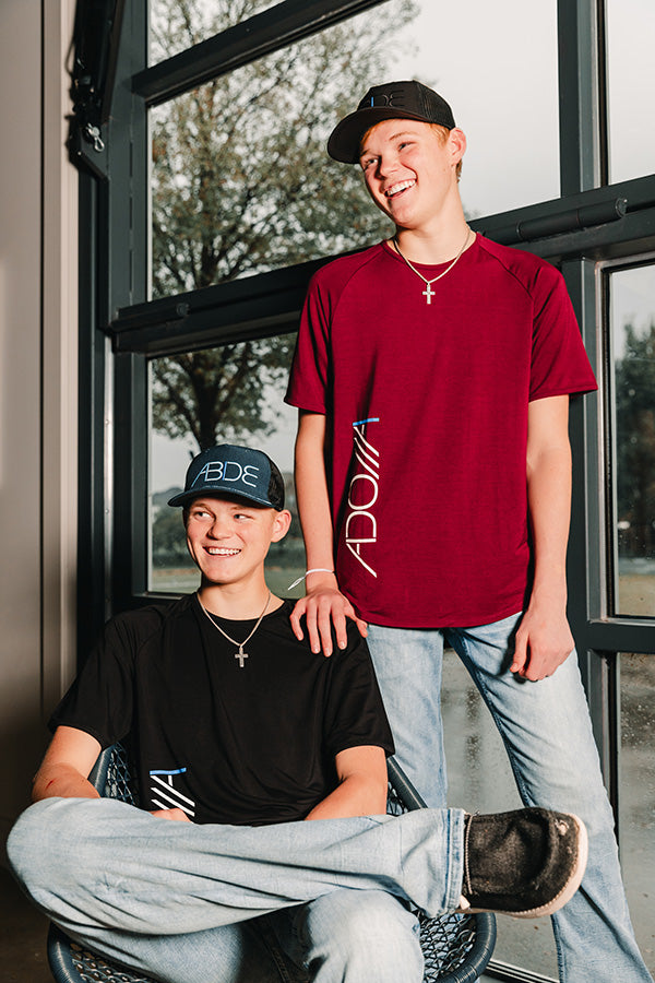 Two Christian Youth infront of garage door wearing complimenting ADONAI Bamboo Tees and ABIDE Trucker Hats