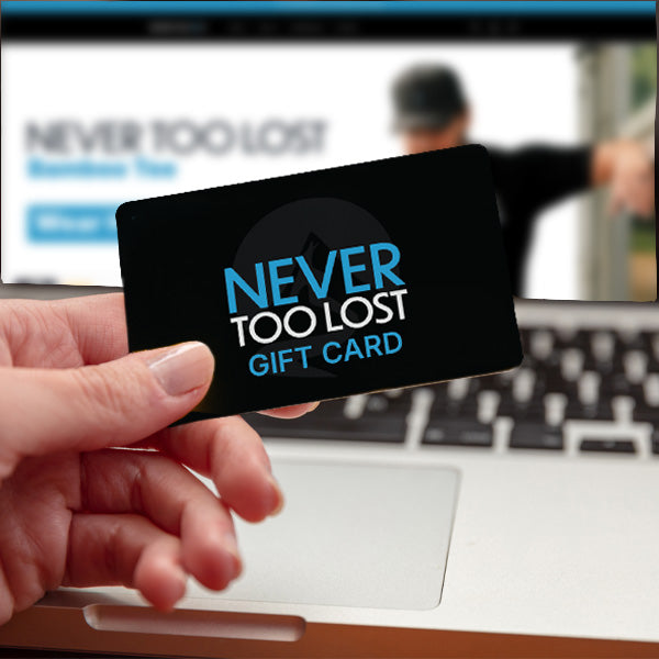 Hand holding Never TOo LOst Gift Card with Laptop in the background with Never Too Lost website in a browser