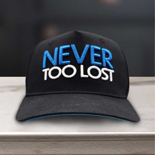 Black cap with 'NEVER TOO LOST' text on front and 'TO BE FOUND' on the back sitting on a marble surface