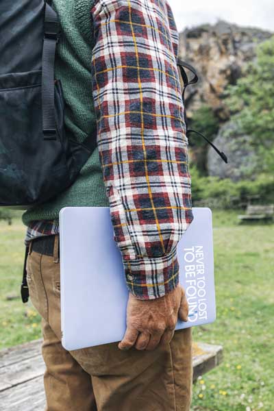 man hiking carrying laptop with Never Too Lost To Be Found sticker on it.