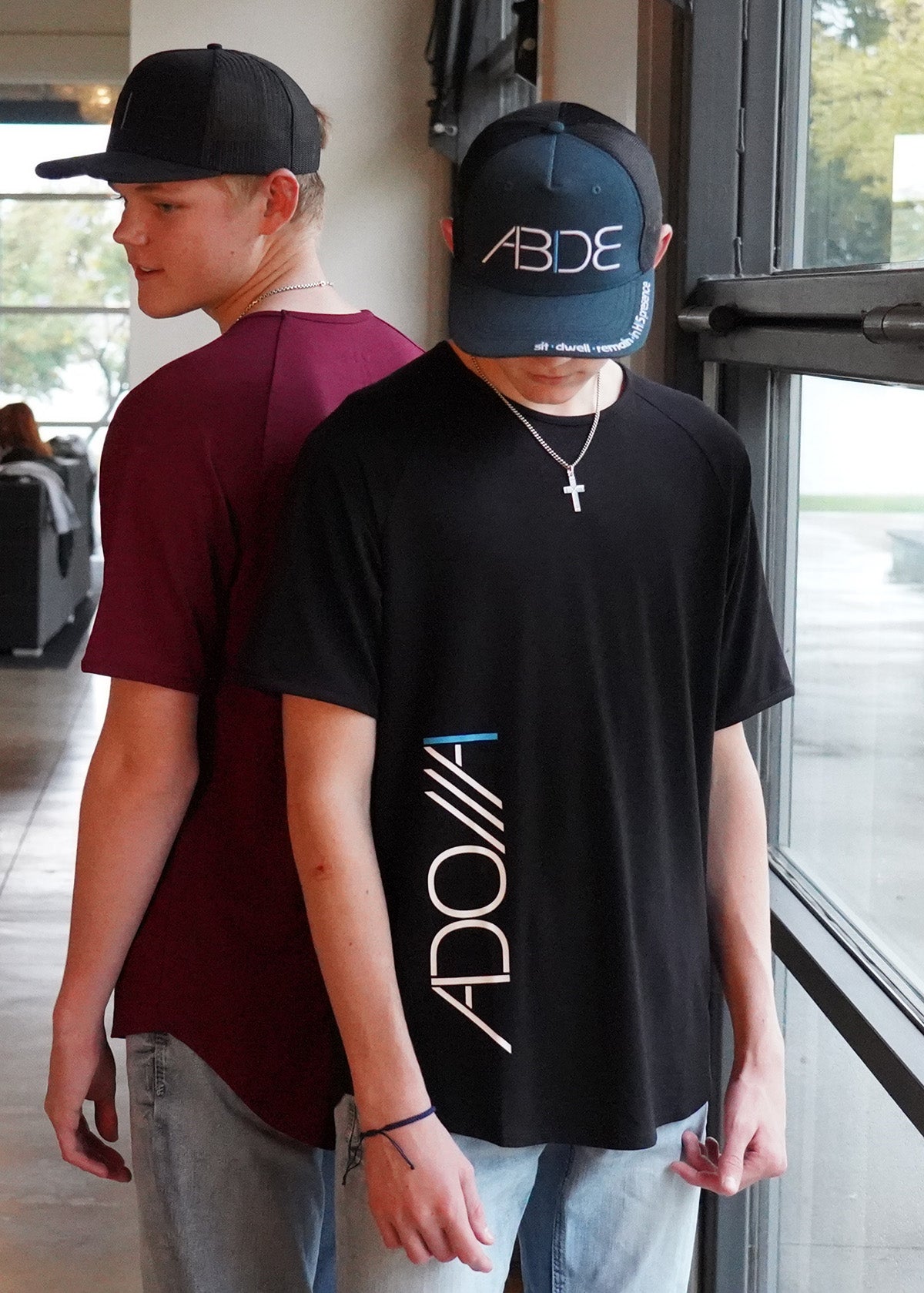 teen boys standing back-to-back wearing now found apparel's "adonai" bamboo tees and "abide" trucker hats, one wearing black facing the camera, the other in wine red