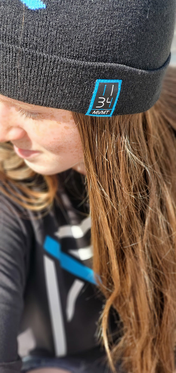 1134 MVMT Logo representing the love of Jesus on a black beanie worn by a young christian woman