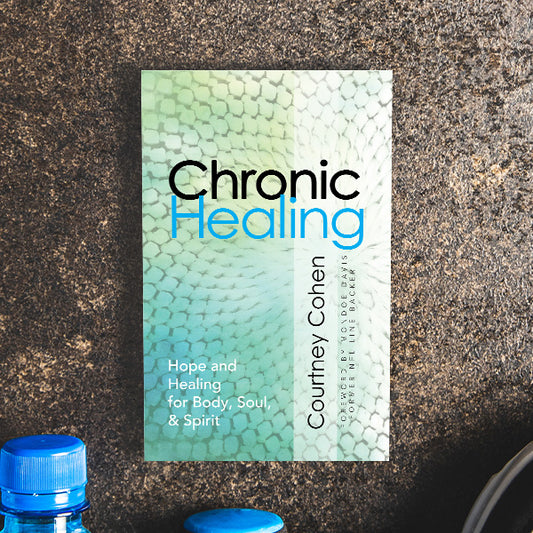 Book titled 'Chronic Healing' by Courtney Cohen on a textured surface with a blue bottle cap in the foreground.