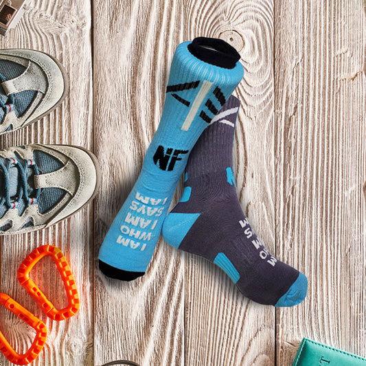 Blue and black I Am Who I AM Says I Am socks on a wooden floor, next to boots.