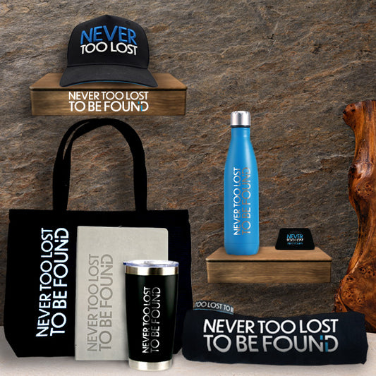 The Abundance Bundle Collection of 'Never Too Lost' branded merchandise including a hat, tote bag, water bottle, and more on a stone background.