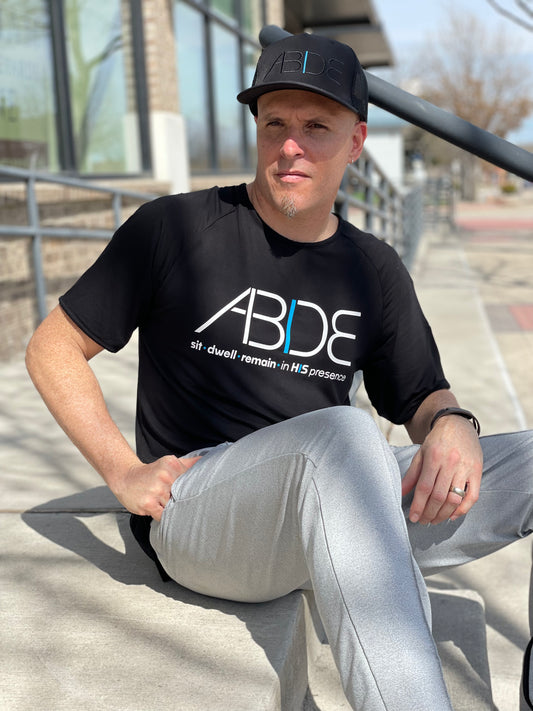 Now Found Co-Founder Steve Cohen sitting on stairs wearing ABIDE Black Trucker Hat and Black ABIDE sit - dwell - remain in His presence bamboo shirt