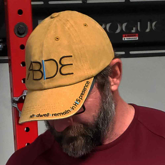A mustard yellow dad hat with the word "Abide" embroidered on the front, sit - dwell - remain in His presence on the bill This is Christian apparel.